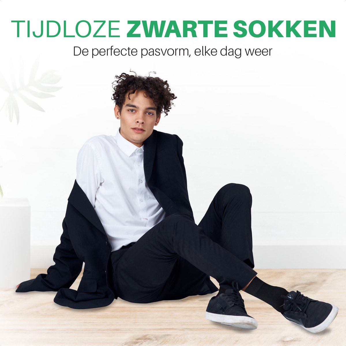 Man in wit overhemd zit op de grond en draagt zwarte bamboe sokken bij donkere sneakers